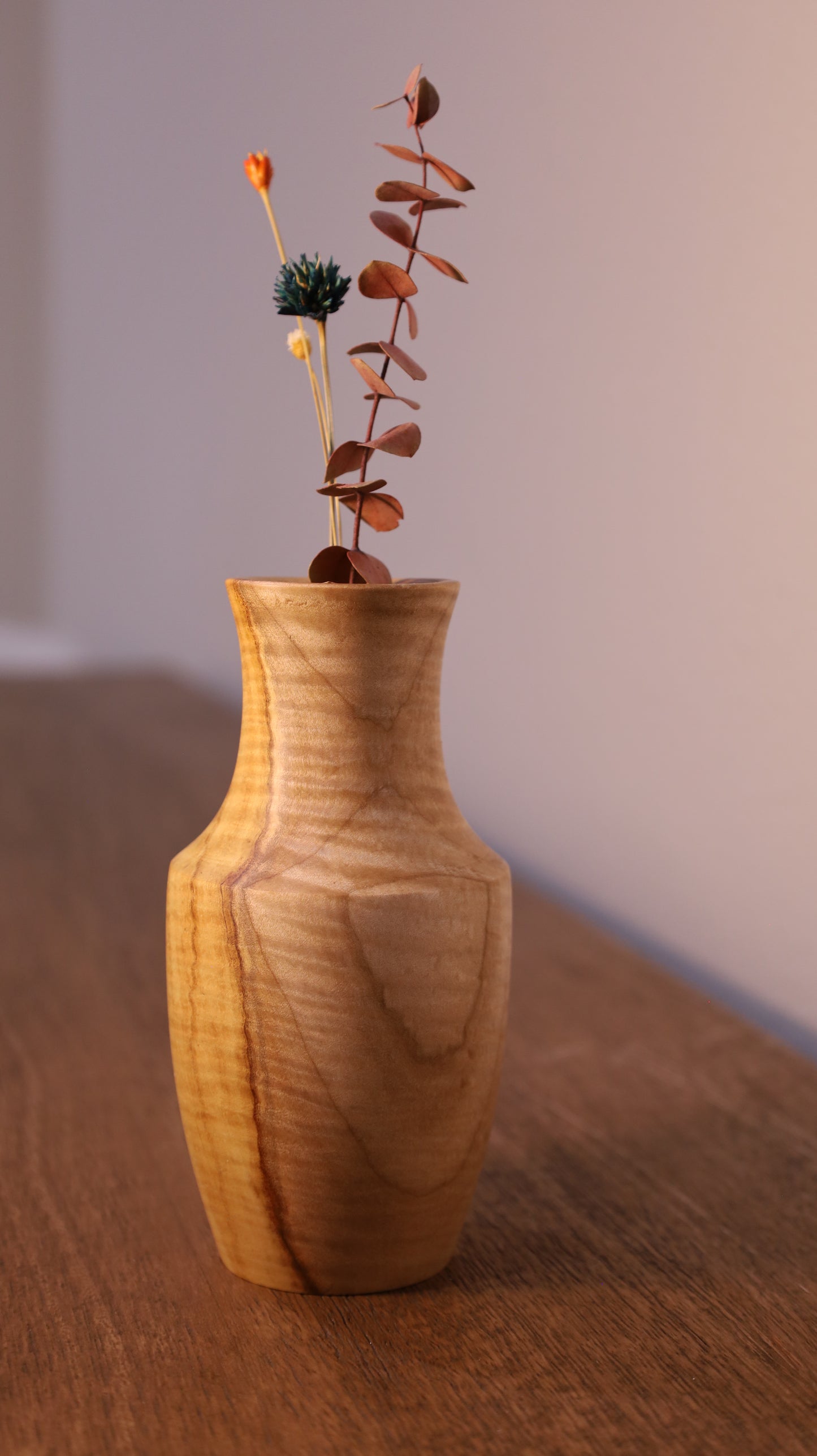 Wooden vase with a branch of dried leaves on a neutral background