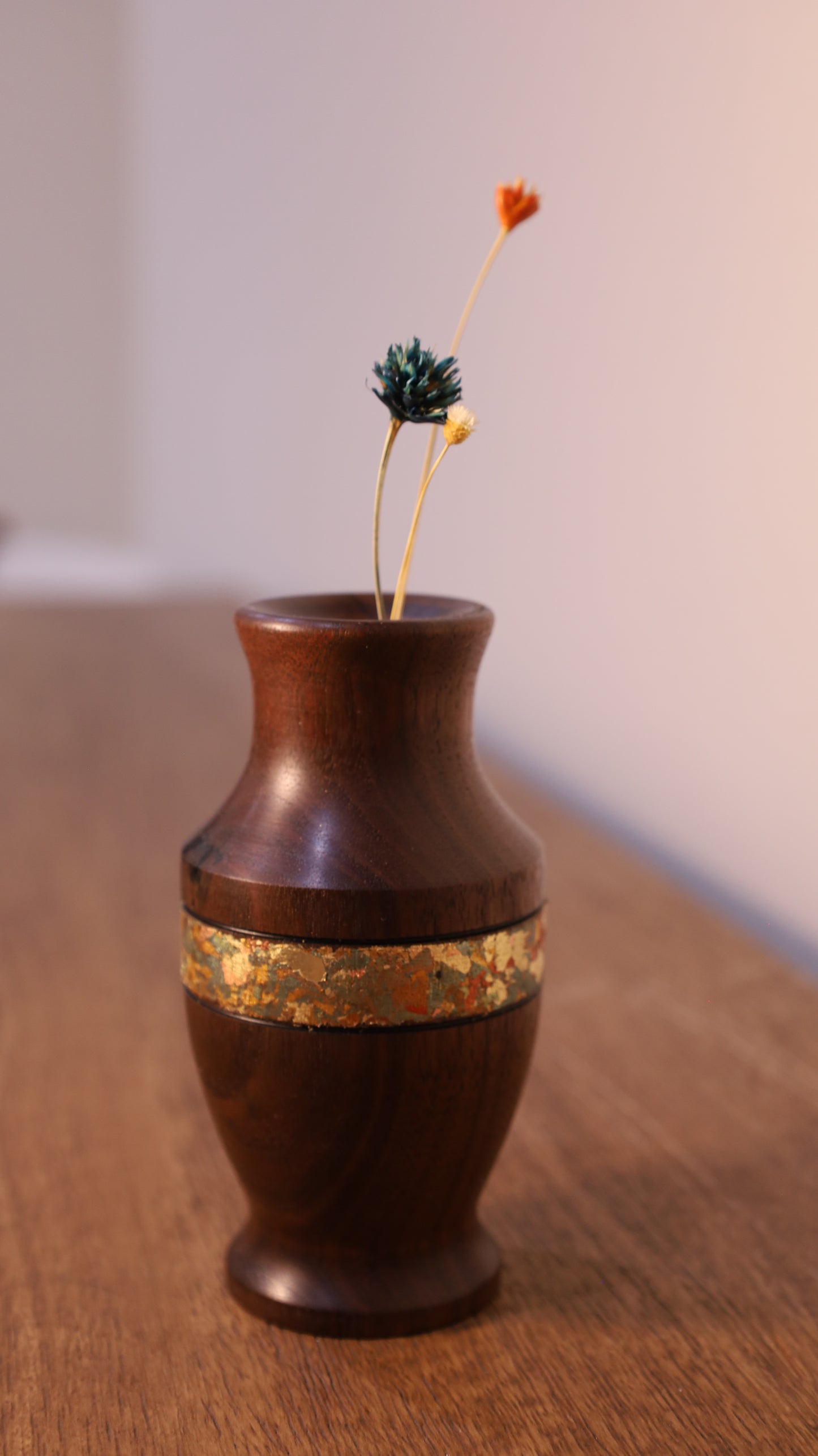Wooden vase with gold band on a wooden surface
