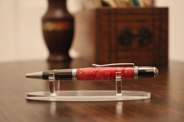 custom Pen with red barrel and silver accents on a clear stand on a wooden surface.