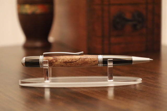 custom pen with gold accents on a clear stand on a wooden surface