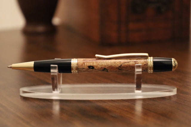 custom wooden Pen with black and gold accents on a clear stand against a blurred background