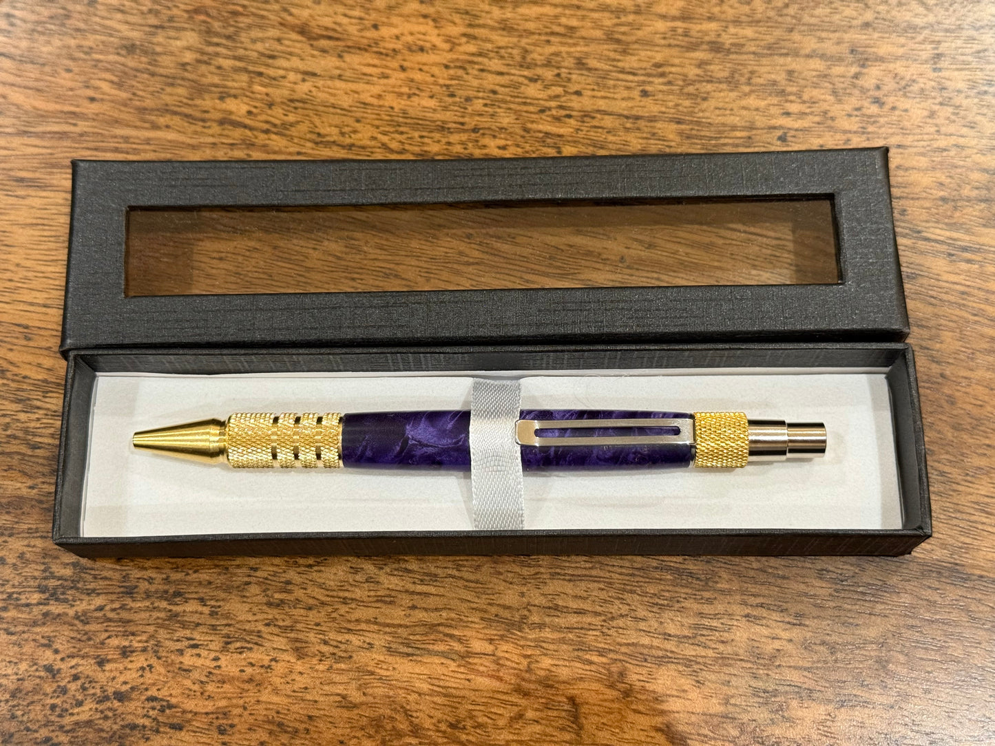 Purple and gold pen in a black box on a wooden surface
