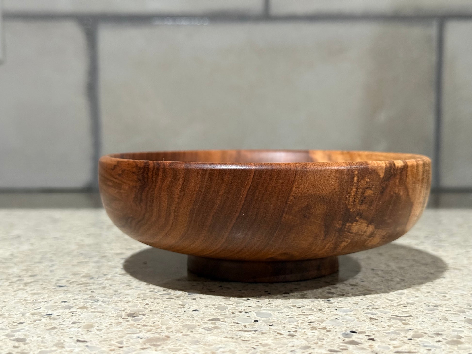 Wooden bowl on a concrete surface with a tiled wall background