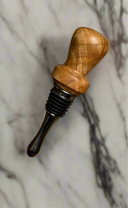A wooden bottle stopper with a maple handle and a metal stopper mechanism, placed on a marble surface.