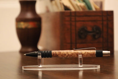 custom Pen with maple burl grip on a clear stand against a blurred backgroundl