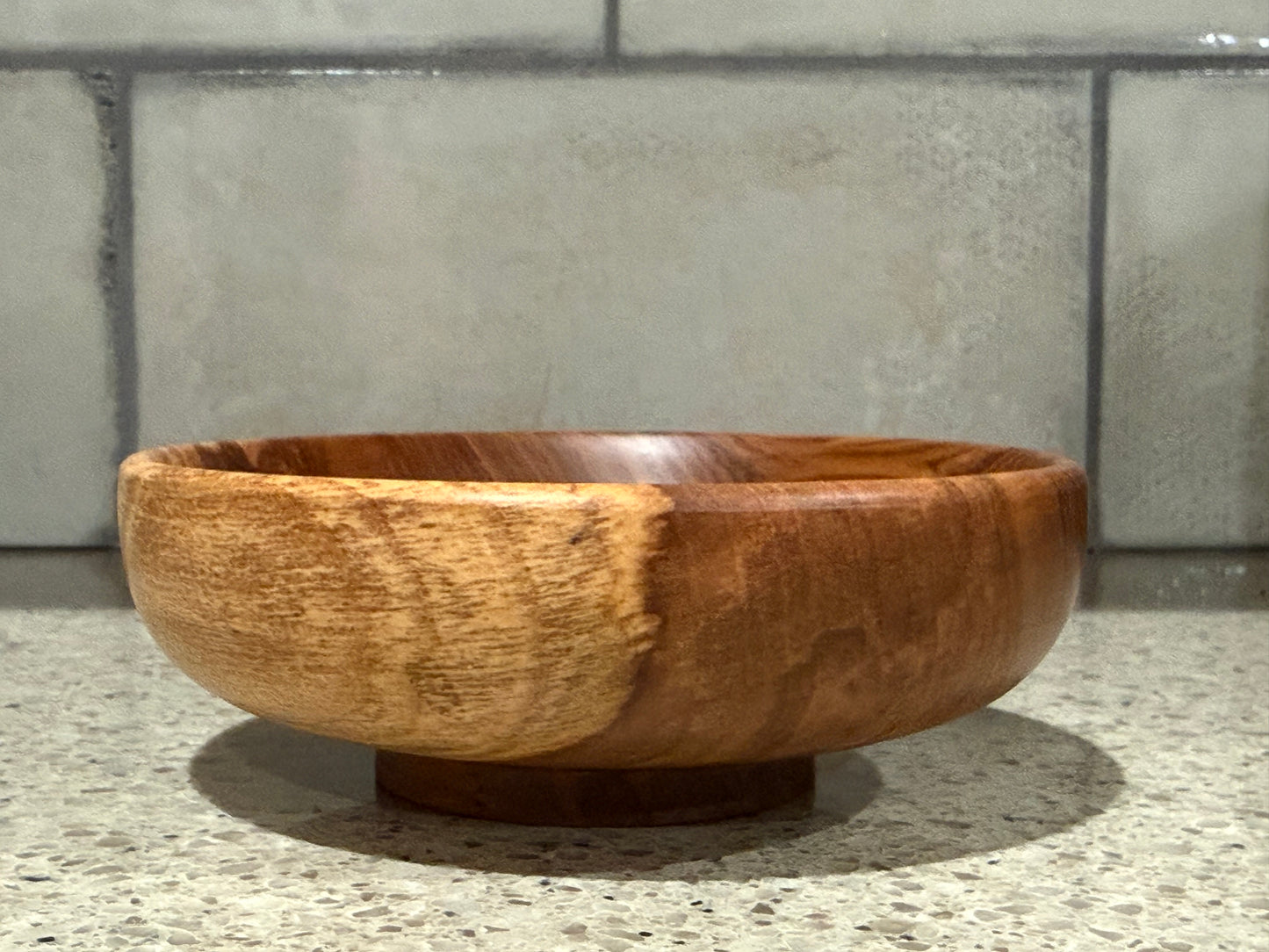 Wooden bowl on a countertop with a tiled wall background