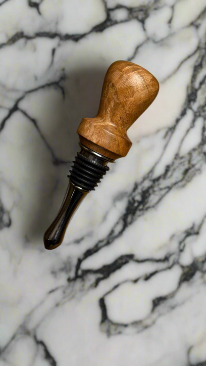 A wooden bottle stopper with a maple handle and a metal stopper mechanism, placed on a marble surface.