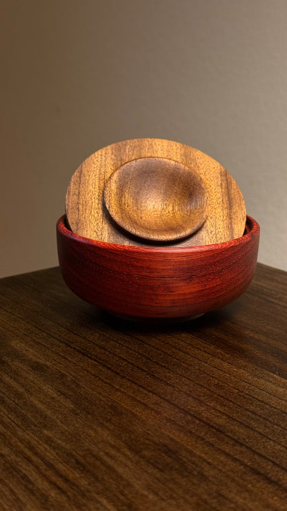 A decorative African lidded ring bowl made of African Padouk wood with a lid made of African Teak, placed on a wooden surface.