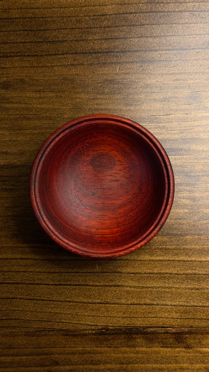 A decorative African lidded ring bowl made of African Padouk wood with a lid made of African Teak, placed on a wooden surface.