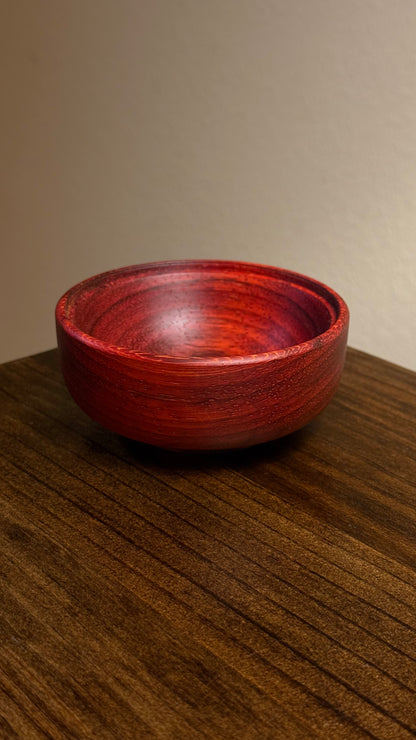 A decorative African lidded ring bowl made of African Padouk wood with a lid made of African Teak, placed on a wooden surface.