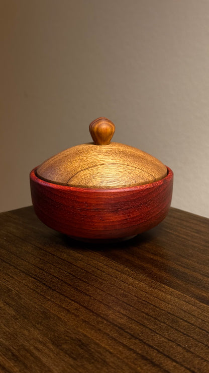 A decorative African lidded ring bowl made of African Padouk wood with a lid made of African Teak, placed on a wooden surface.