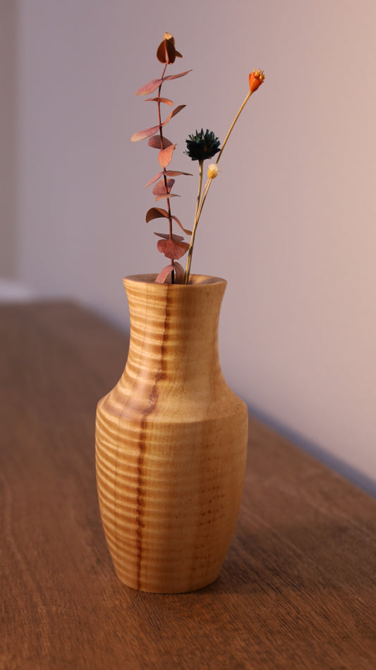 Wooden vase with a branch of dried leaves on a wooden surface