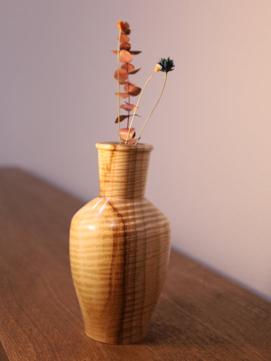 Wooden vase with a decorative twig on a wooden surface