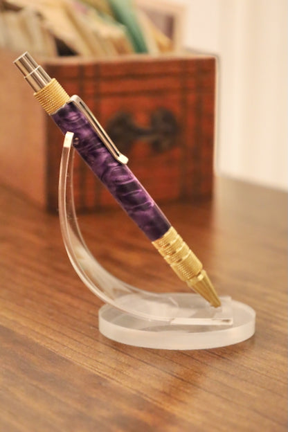 Purple and gold pen on a clear stand with a blurred background. Custom pen