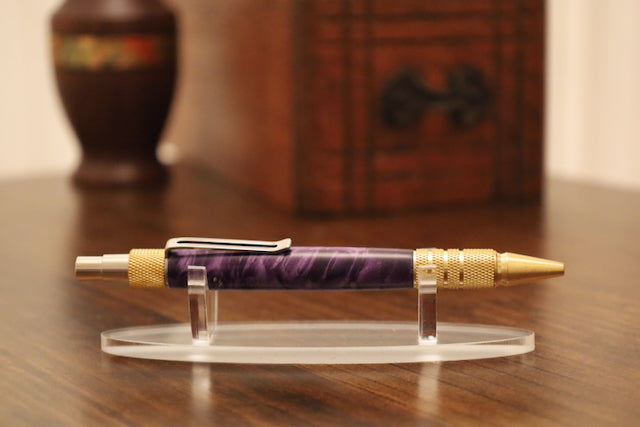 Purple pen with gold accents on a clear stand against a wooden background custom pen

