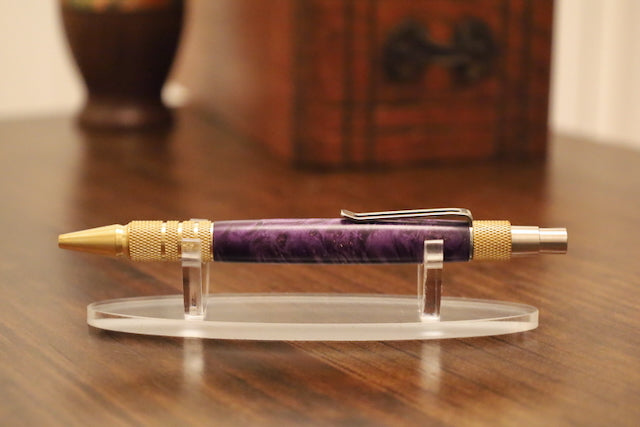 Purple pen with gold accents on a clear stand on a wooden surface custom pen