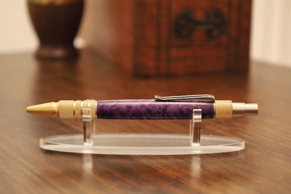 Purple pen with gold accents on a clear stand on a wooden surface custom pen