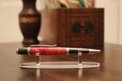 custom Pen with red barrel and silver accents on a clear stand on a wooden surface.