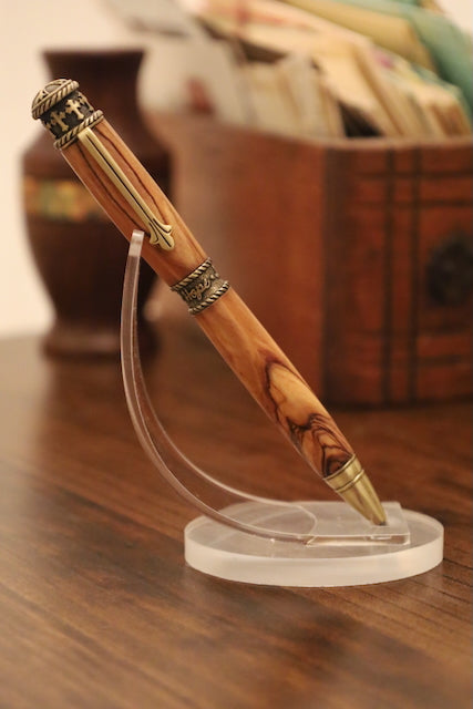 Wooden pen with gold accents on a clear stand on a wooden surface