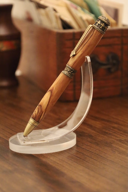 Wooden pen with decorative elements on a clear stand against a blurred background