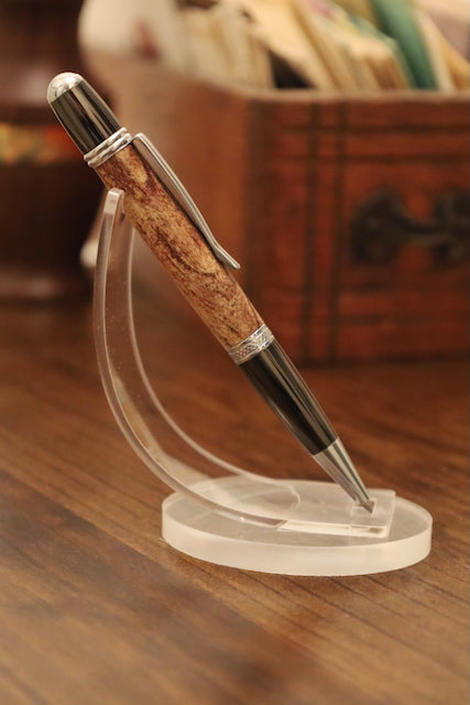 custom pen with gold accents on a clear stand on a wooden surface