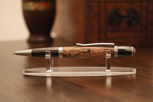 custom pen with gold accents on a clear stand on a wooden surface