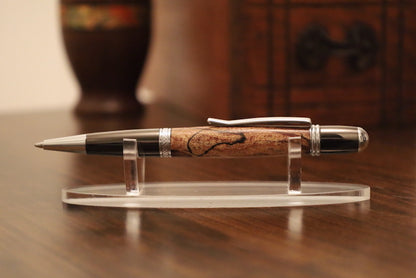custom pen with gold accents on a clear stand on a wooden surface