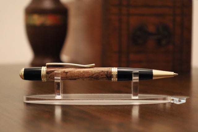 custom  wooden Pen with black and gold accents on a clear stand against a blurred background