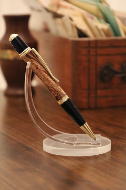 custom  wooden Pen with black and gold accents on a clear stand against a blurred background