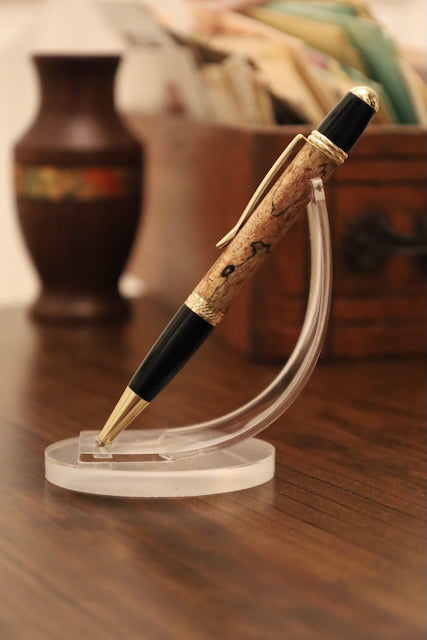 custom  wooden Pen with black and gold accents on a clear stand against a blurred background