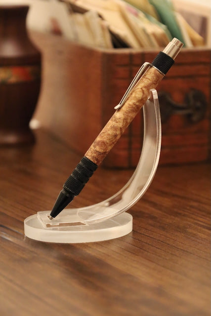 custom Pen with maple burl grip on a clear stand against a blurred backgroundl