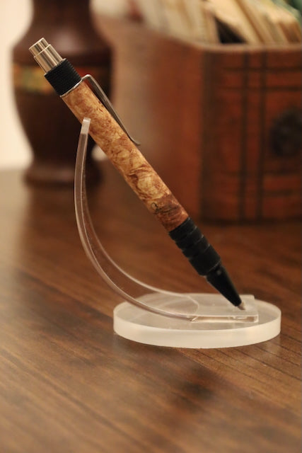 custom Pen with maple burl grip on a clear stand against a blurred backgroundl