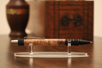 custom Pen with maple burl grip on a clear stand against a blurred backgroundl