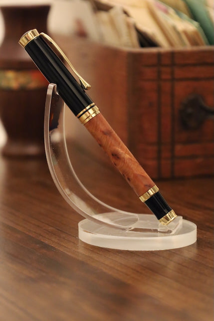Pen with wooden grip and gold accents on a clear stand against a blurred background