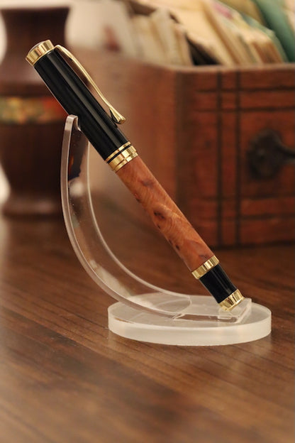 Pen with wooden grip and gold accents on a clear stand against a blurred background