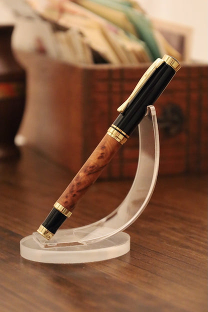 Pen with wooden grip and gold accents on a clear stand