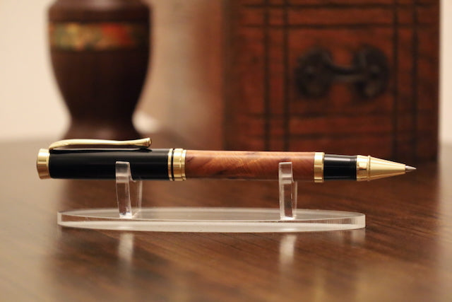 Wooden pen with gold accents on a clear stand against a wooden background