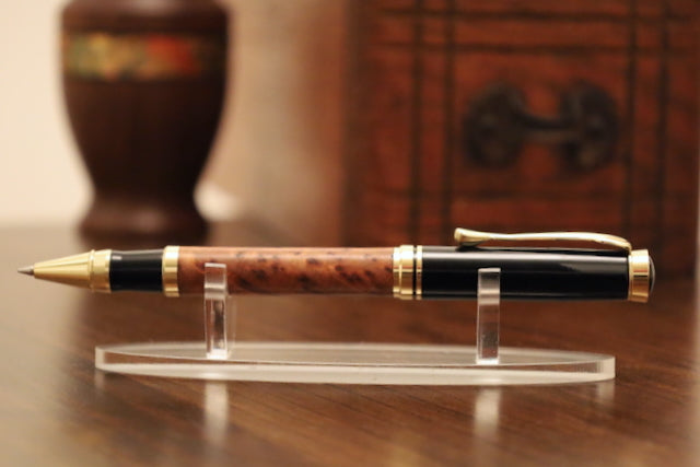 Wooden pen with gold accents on a clear stand against a wooden background