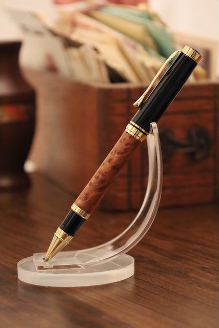 Luxury pen with wooden barrel and gold accents on a clear stand, blurred background