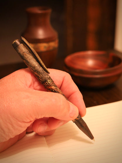 Hand holding a textured pen with a blurred background of wood items
