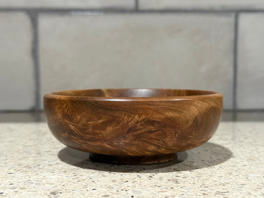 Wooden bowl on a speckled countertop with a tiled wall background