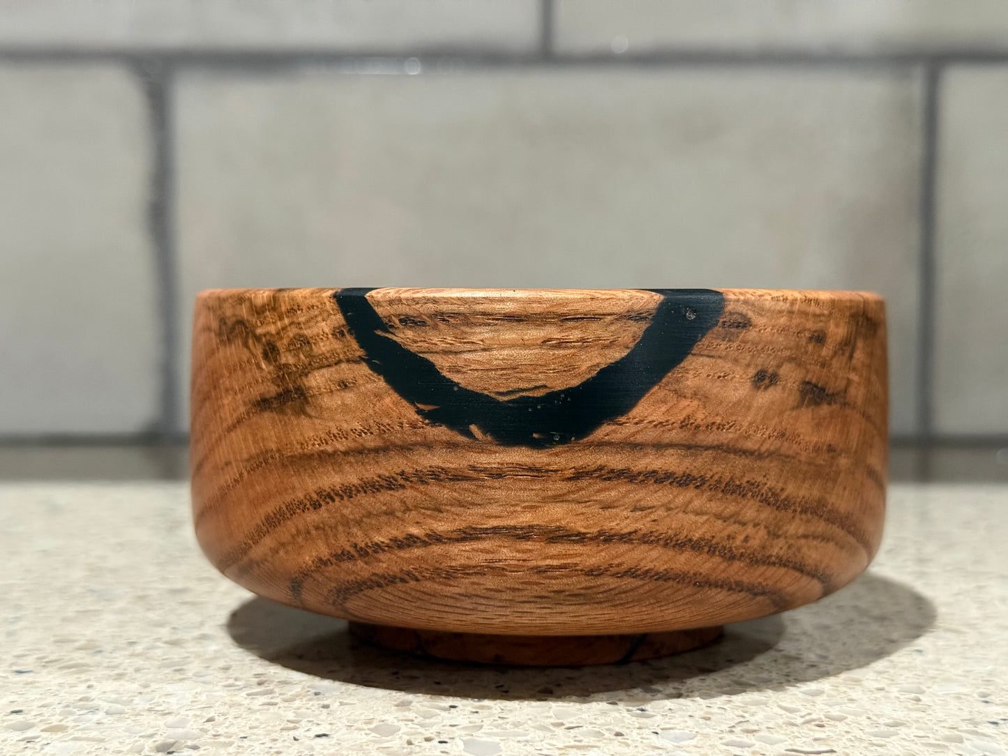 Wooden bowl with a black interior on a kitchen counter with a tiled wall background