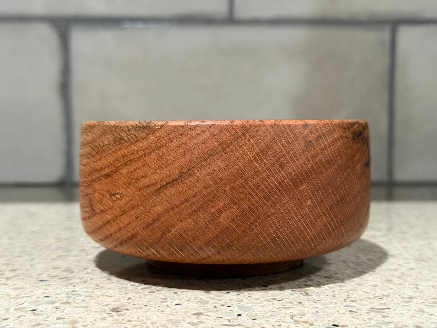 Wooden bowl with a black interior on a kitchen counter with a tiled wall background