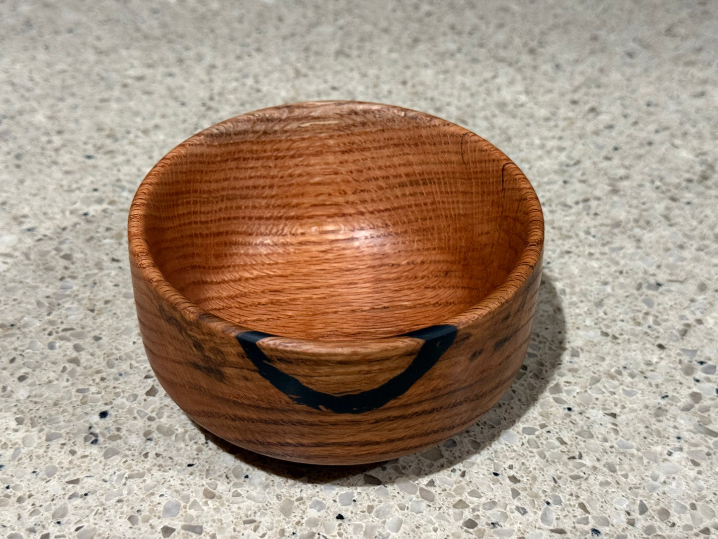 Wooden bowl with a black interior on a kitchen counter with a tiled wall background