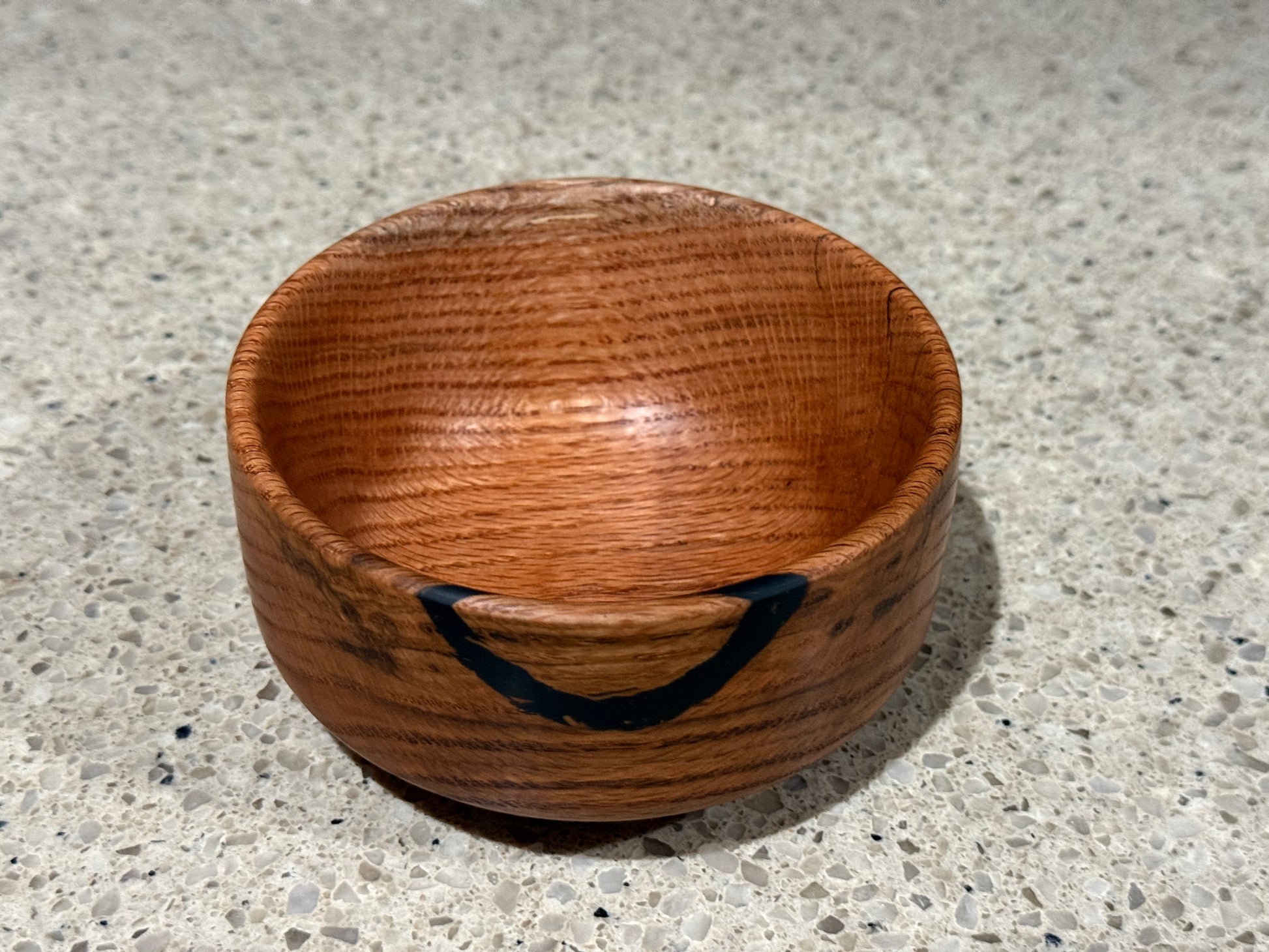 Wooden bowl with a black interior on a kitchen counter with a tiled wall background