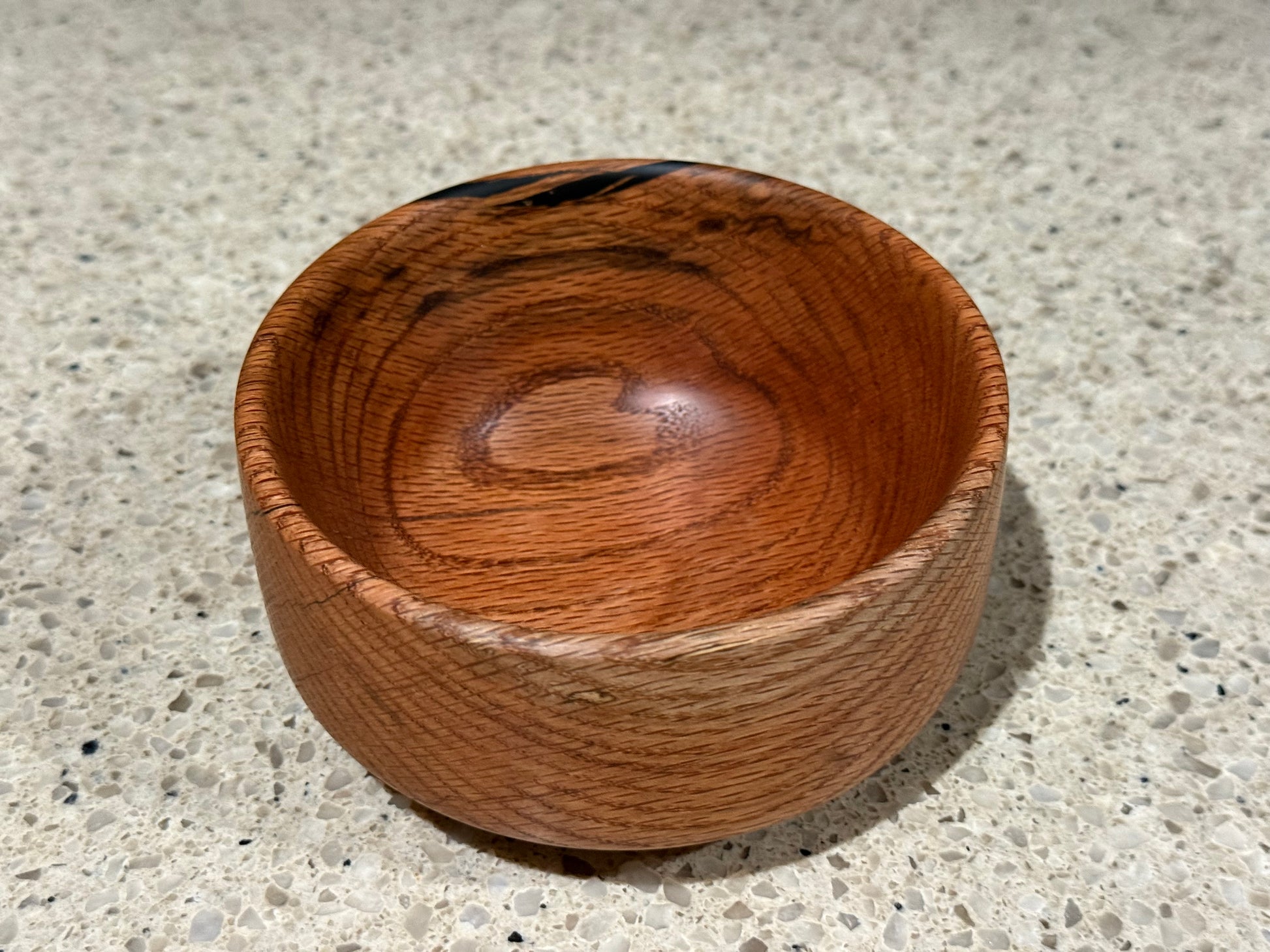 Wooden bowl with a black interior on a kitchen counter with a tiled wall background