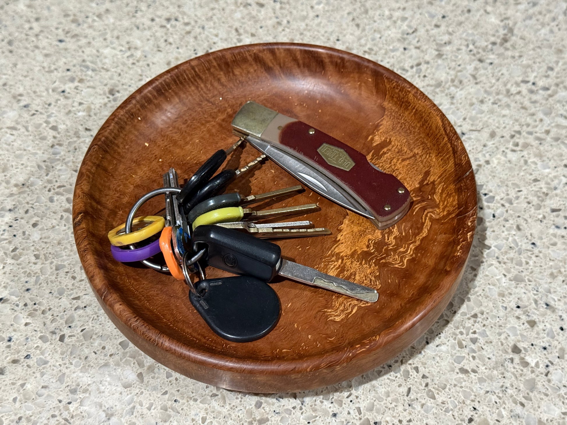 Wooden bowl with keys and a pocket knife on a klitchen counter